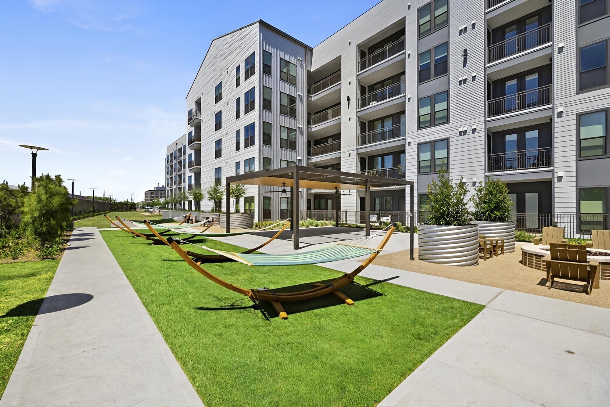 A modern apartment building with multiple balconies, a covered outdoor seating area, and a well-maintained lawn with hammocks.