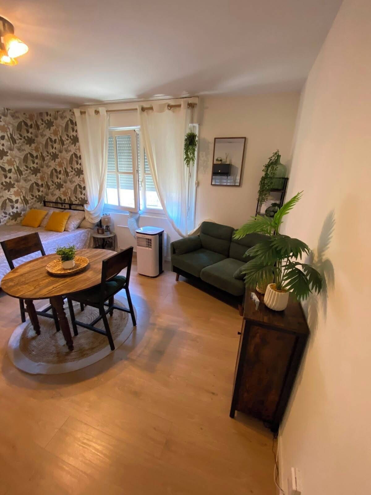A living room with a sofa, a dining table with chairs, a small table with a lamp, and a potted plant.