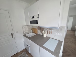 A compact kitchen with white cabinetry, a built-in microwave, a sink, and a countertop with a paper holder. - Beautiful 1-bedroom apartment in Paris perfect for your getaway (Paris)