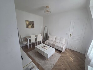 A modern, minimalist living room with a white sofa, a dining table with chairs, a coffee table, and a large mirror. - Beautiful 1-bedroom apartment in Paris perfect for your getaway (Paris)