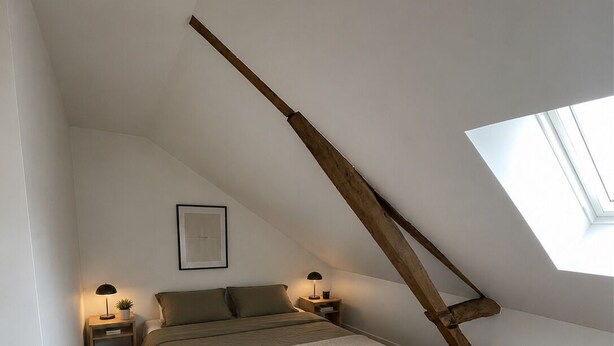 A bedroom with a sloped ceiling, a skylight, a bed with a headboard, bedside tables with lamps, and a framed picture on the wall.