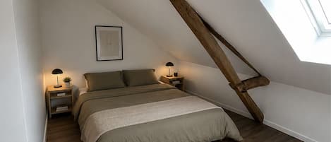 A bedroom with a sloped ceiling, a skylight, a bed with a headboard, bedside tables with lamps, and a framed picture on the wall.