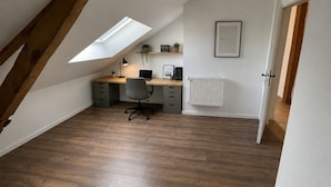 A room with a sloped ceiling, a desk with a chair, a radiator, and a framed picture on the wall. - Gite des Chemins de la Paillardiere (Saint-M'Hervé)