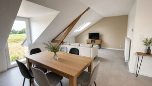 A modern loft-style living space with a dining area, a sofa, a television, and a view of the outdoors. - Gite des Chemins de la Paillardiere (Saint-M'Hervé)