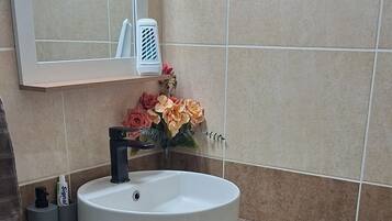 A bathroom with a round sink, a mirror, a trash bin, and a green rug.