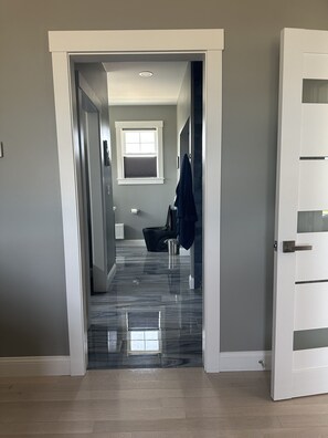 Um corredor com porta para banheiro, janela e piso ladrilhado.