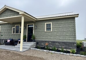 Ein zweigeschossiges Haus mit überdachter Veranda, Steinstufen und einem angelegten Garten.