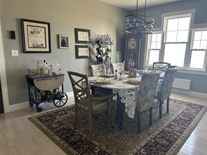 A dining room with a table set for six, surrounded by patterned chairs, a decorative chandelier, and wall-mounted artwork. - Oceanfront Gorgeous  2-bedroom house in charming Perry, ME, perfect for relaxing (Perry)