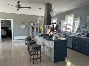 A modern kitchen with a central island, bar stools, and a dining area with a bed. - Oceanfront Gorgeous  2-bedroom house in charming Perry, ME, perfect for relaxing (Perry)