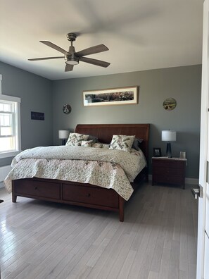 Ein Schlafzimmer mit einem Bett, einem Nachttisch, einem Deckenventilator und einem Fenster.