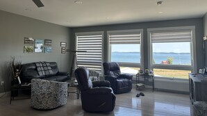 En moderne stue med havudsigt, med ventilator i loftet, store vinduer og en lædersofa.