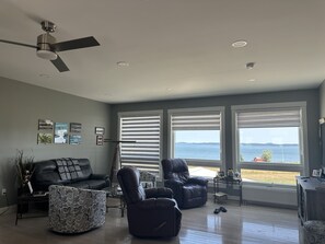 Ein modernes Wohnzimmer mit Meerblick, ausgestattet mit einem Deckenventilator, großen Fenstern und einem Ledersofa.