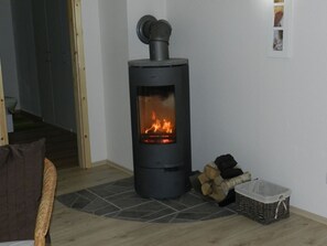 A room with a wood-burning stove, a wicker chair, and a small table. - A light-filled, modern vacation home in the Nordheide (Fintel)