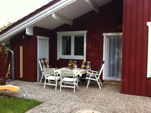 A covered outdoor seating area with a table and chairs, a window, and a door. - A light-filled, modern vacation home in the Nordheide (Fintel)
