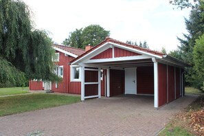 A red building with a covered garage and a brick pathway leading to the entrance. - A light-filled, modern vacation home in the Nordheide (Fintel)