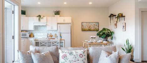 A modern living room with a sofa, a dining table, and a kitchen in the background.