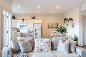 A modern living room with a sofa, a dining table, and a kitchen in the background.