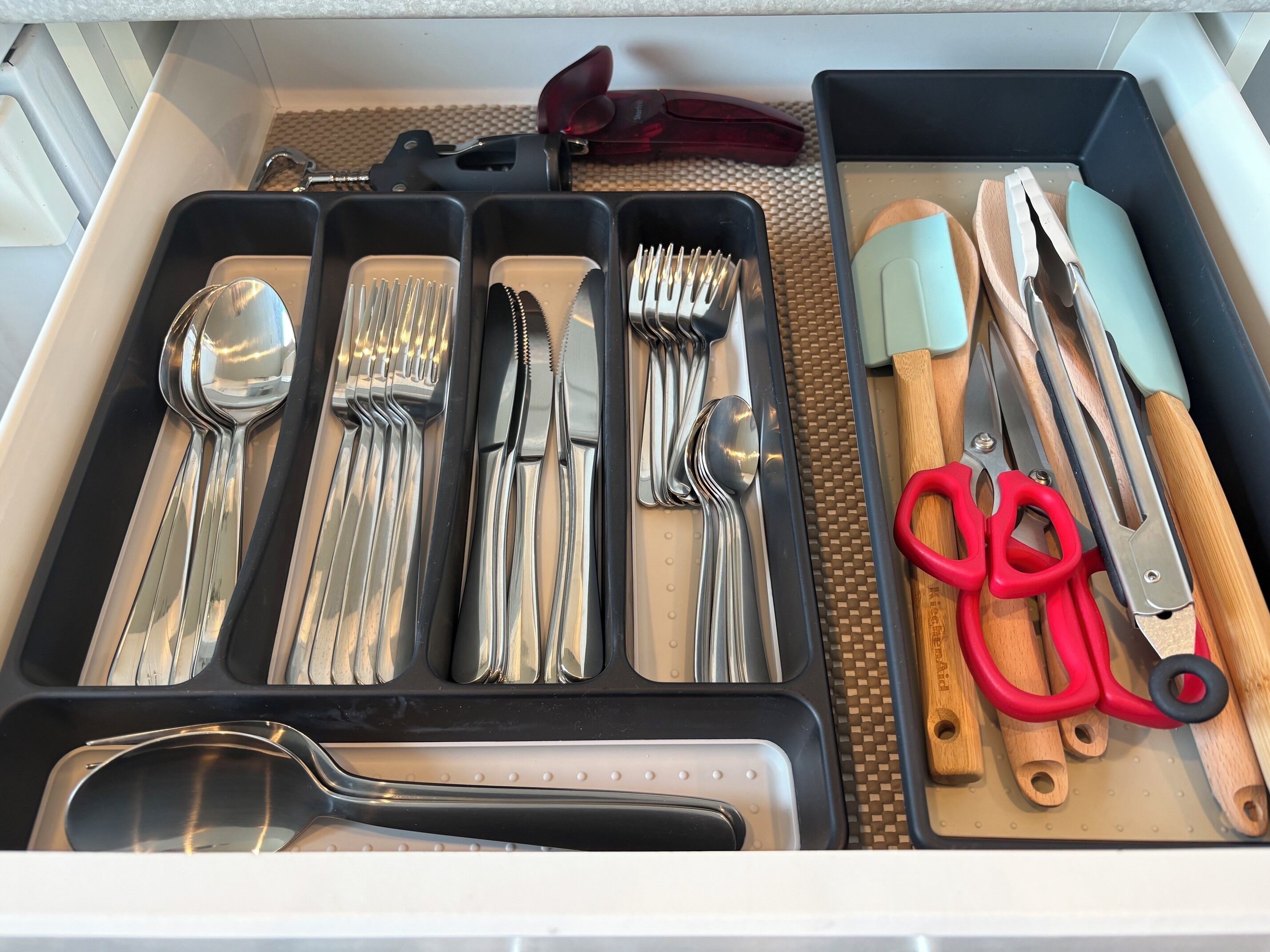 A drawer containing various kitchen utensils including forks, knives, spoons, and scissors.
