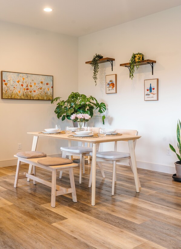 Comedor con una mesa de madera dispuesta para cuatro personas, rodeado de sillas con cojines.