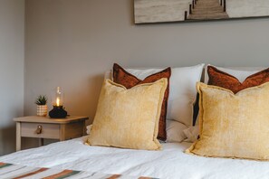 A bed with two pillows, a bedside table with a lamp, and a wall-mounted artwork.