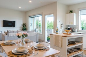 A modern kitchen with a dining area, large windows, and a flat-screen TV mounted on the wall.
