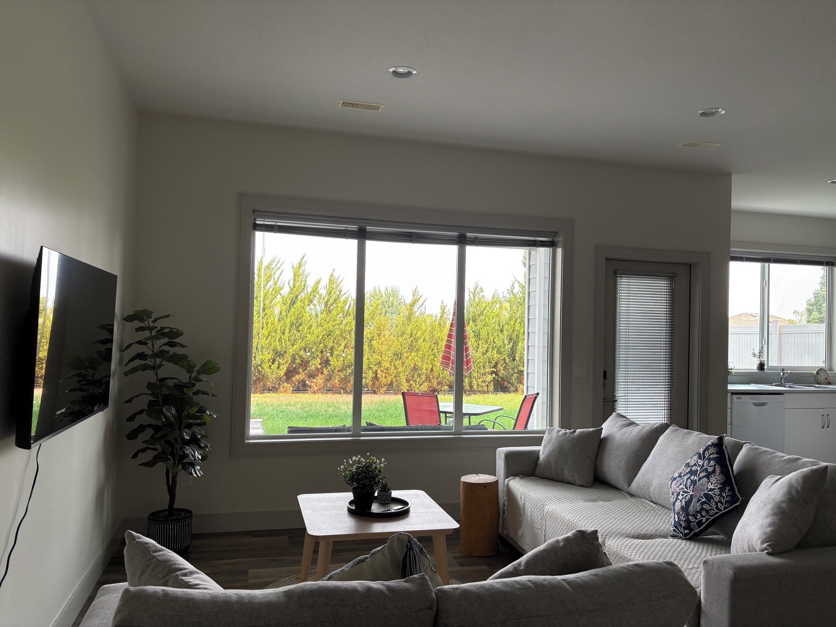 A modern living room with a large window, a sofa, a small table, and a potted plant.