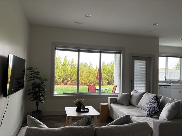 A modern living room with a large window, a sofa, a small table, and a potted plant.