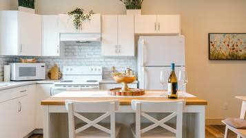 A modern kitchen with white cabinetry, a central island with chairs, a stove, and a refrigerator.