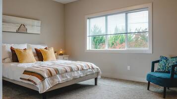 A bedroom with a large bed, a nightstand, a chair, and a window with blinds.