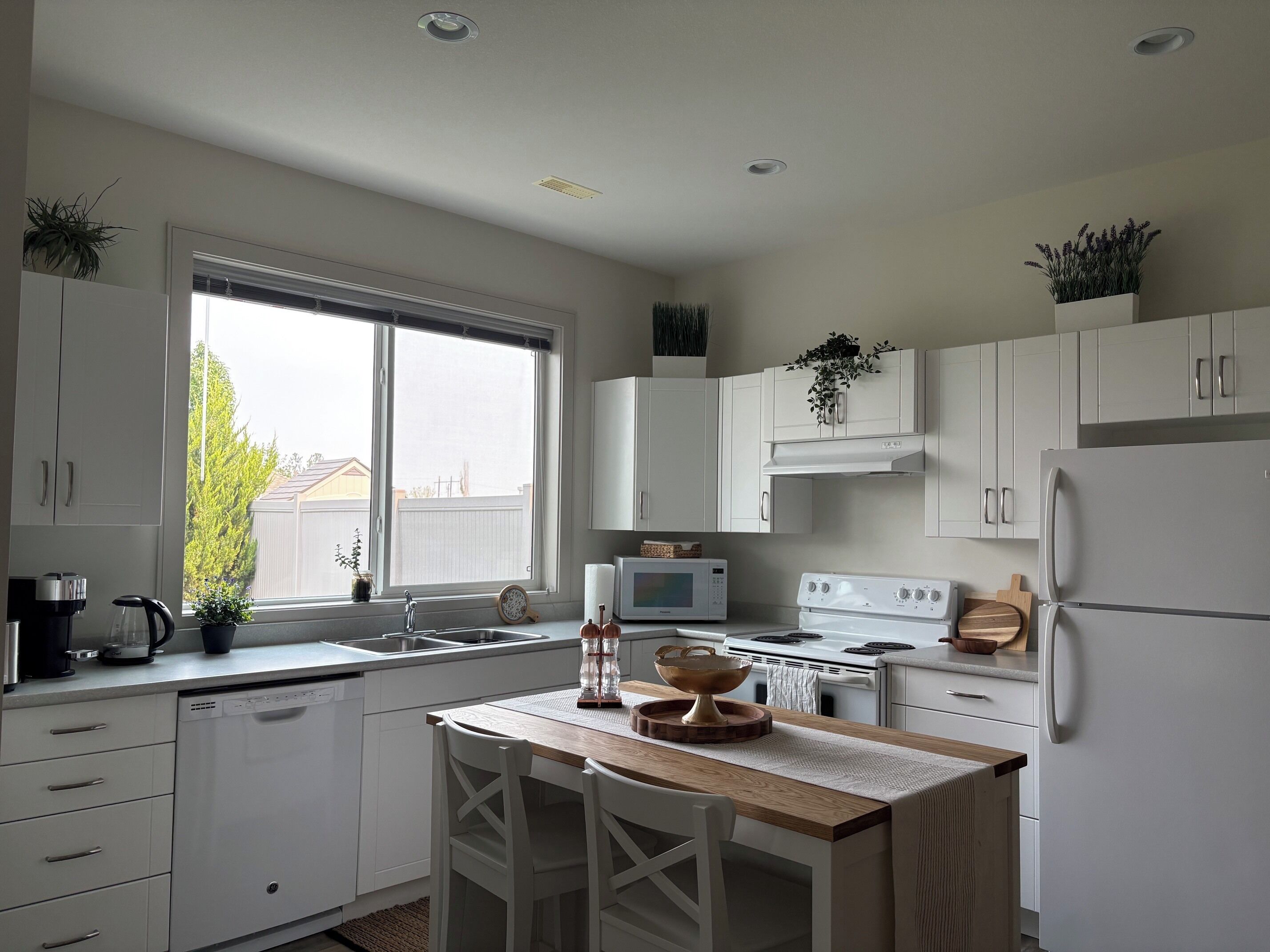 A modern kitchen with white cabinetry, a wooden island, and a view of the outside through a large window.