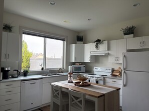 A modern kitchen with white cabinetry, a wooden island, and a view of the outside through a large window.