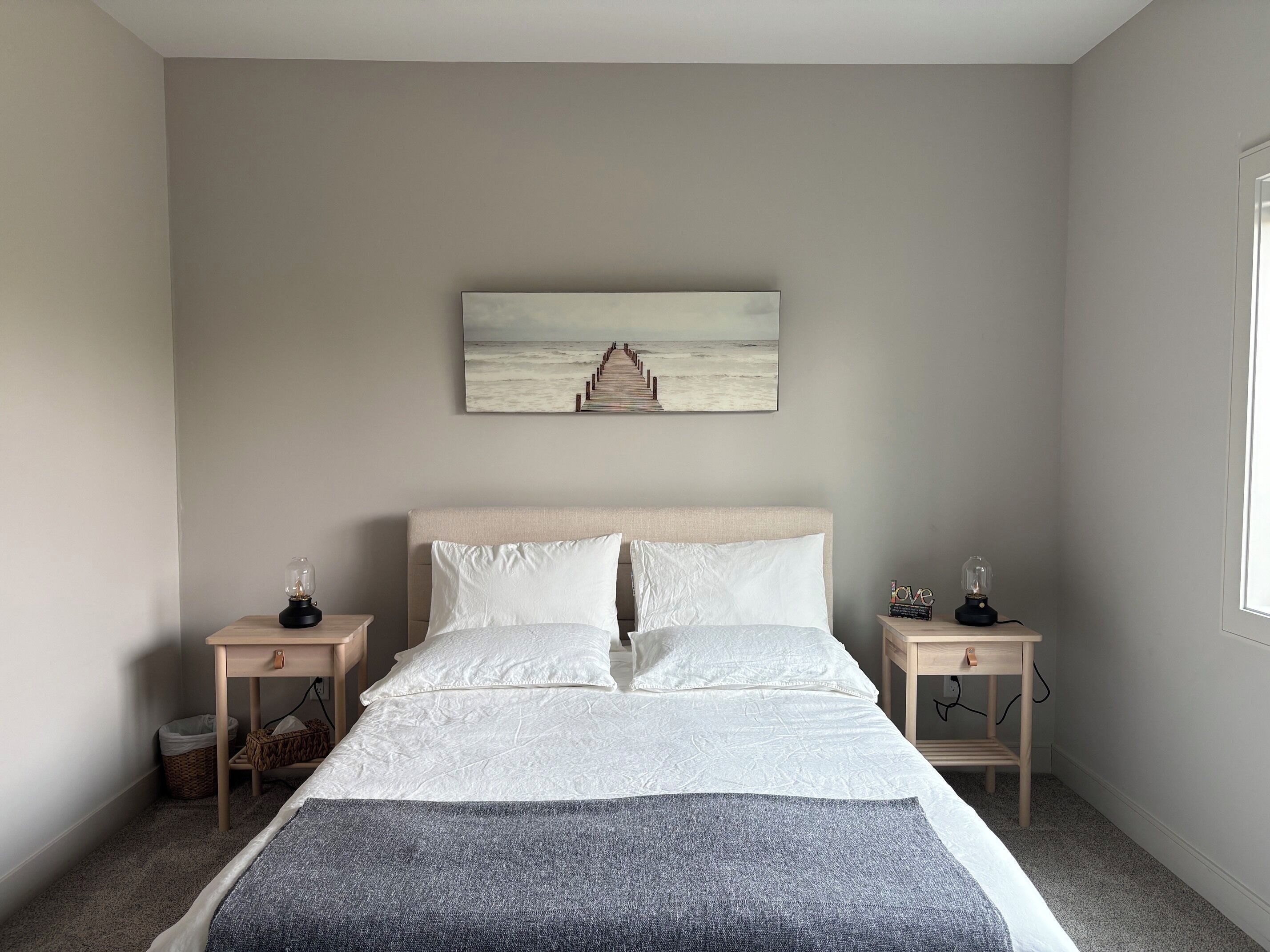 A bedroom with a bed, two bedside tables, a wall-mounted picture, and a window.