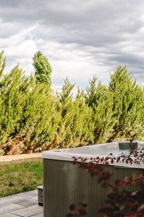 A hot tub with a wooden exterior, surrounded by a grassy area and dense coniferous trees.