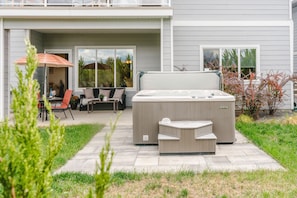 A patio with a hot tub, outdoor furniture, and a view of the house.