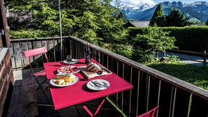 An outdoor dining area with a table set for a meal, surrounded by a wooden deck and a mountain view.
