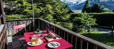An outdoor dining area with a table set for a meal, surrounded by a wooden deck and a mountain view.