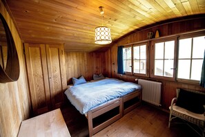 A wooden cabin bedroom with a bed, a chair, a table, and a window.