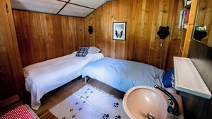 A room with two beds, a wooden ceiling, a framed picture on the wall, a sink, and a mirror.