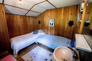 A room with two beds, a wooden ceiling, a framed picture on the wall, a sink, and a mirror.