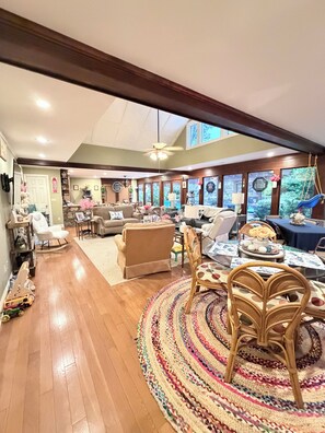 A spacious living room with a high ceiling, wooden beams, a large window, and a ceiling fan. - Less than 1 Mile From the Square and Campus- Huge Sunroom- Sleeps 9 (Oxford)