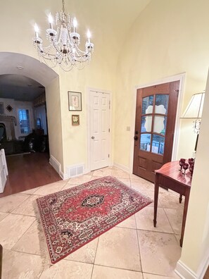 A hallway with a chandelier, a wooden door, a rug, and a table with glasses. - Less than 1 Mile From the Square and Campus- Huge Sunroom- Sleeps 9 (Oxford)