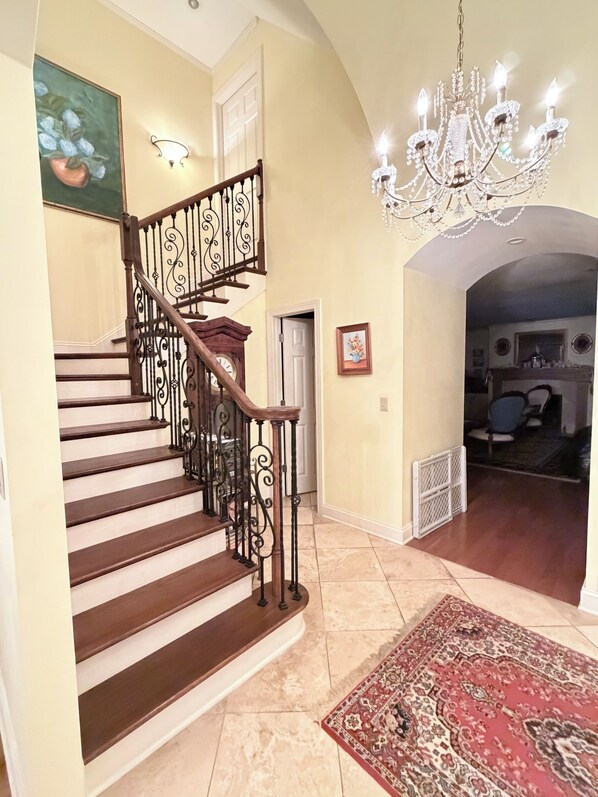 Una gran escalera con barandillas ornamentadas, un candelabro y un tapete estampado.