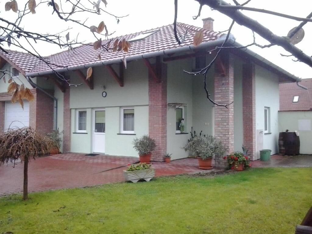 Um edifício residencial com telhado telhado, colunas de tijolo e varanda frontal com plantas em vasos.