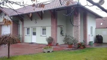 Um edifício residencial com telhado telhado, colunas de tijolo e varanda frontal com plantas em vasos.