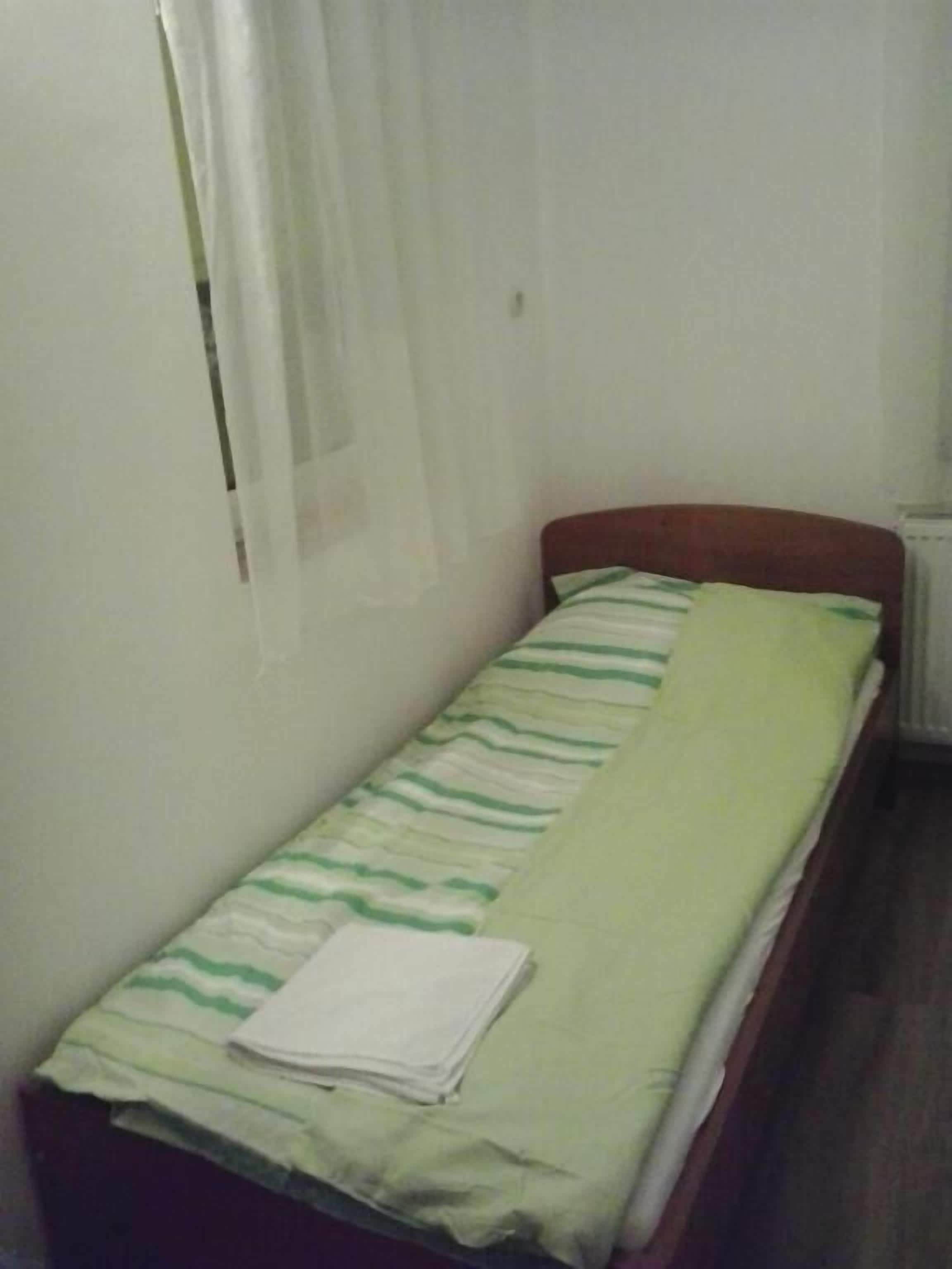 Una cama individual con una colcha verde y blanca a rayas y una toalla blanca doblada.