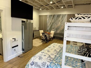 A hotel room with a bunk bed, a desk with a chair, a television, a minibar, and a marble-patterned wall.