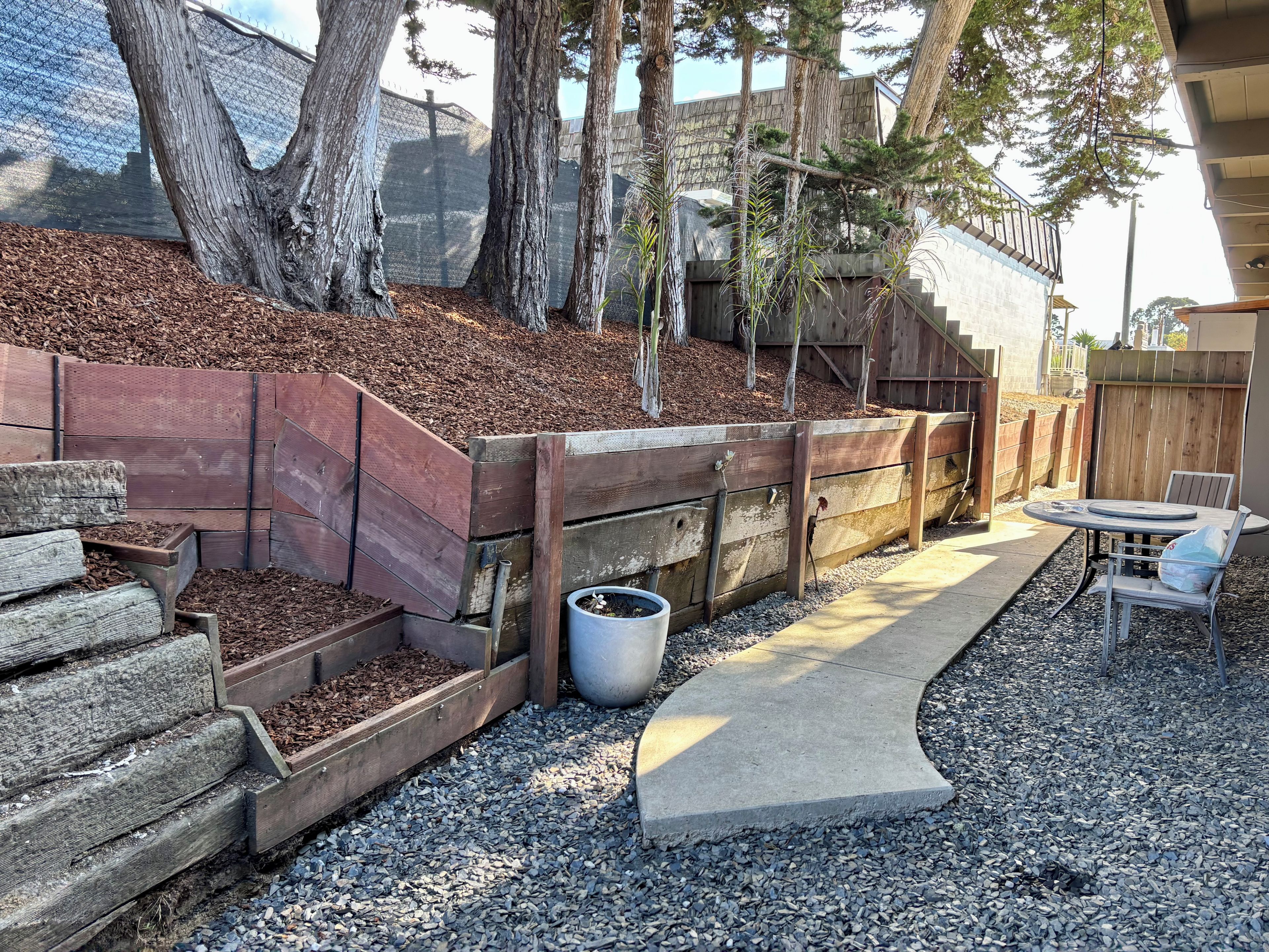 Un espace jardin agrémenté d’un banc en bois, d’un chemin en béton et d’une clôture en bois.