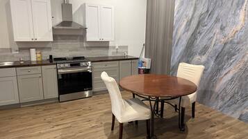 Une cuisine moderne dotée d’appareils électroménagers en acier inoxydable, un coin repas agrémenté d’un mur en marbre, et un plancher en bois.
