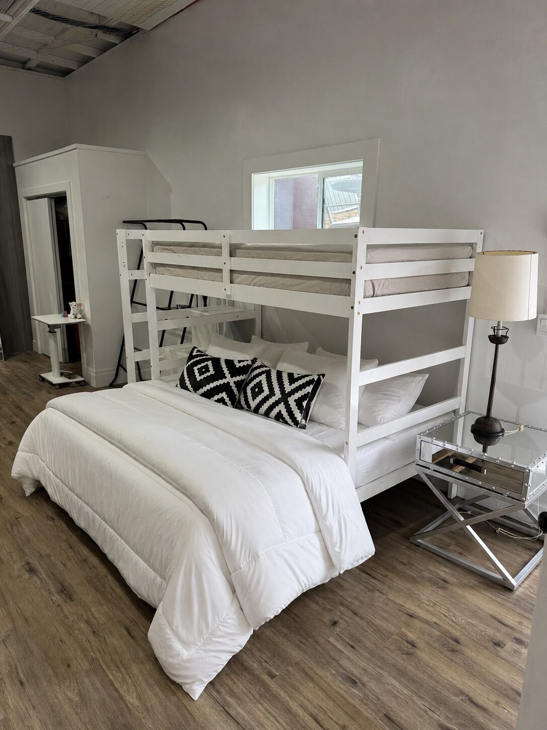 Un lit superposé avec un ensemble de literie blanc, une petite table de chevet et une lampe.