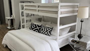 Un lit superposé avec un ensemble de literie blanc, une petite table de chevet et une lampe.